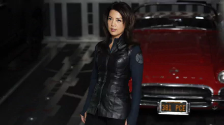 Agents of S.H.I.E.L.D. TV show 2K Quad HD PC desktop wallpaper: a female agent in a dark tactical jacket standing before a red vintage car inside a dim garage.