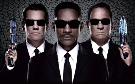 HD PC desktop wallpaper featuring Tommy Lee Jones and Will Smith as agents from Men In Black 3, each holding futuristic weapons against a patterned backdrop.