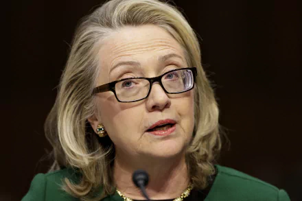 Portrait of Hillary Rodham Clinton, featuring her wearing glasses and a green blazer, captured in a moment of speaking. This image serves as a vibrant HD desktop wallpaper.