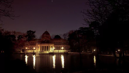 Night view of the man-made Palacio de Cristal illuminated by warm lights, reflected in the pond — HD PC desktop wallpaper and background.