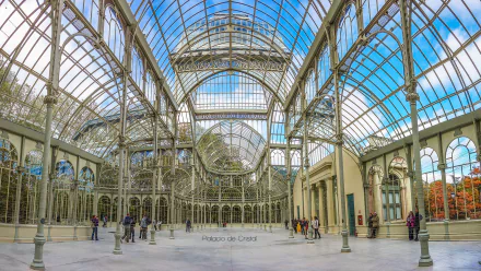 HD PC desktop wallpaper of Palacio de Cristal's ornate glass-and-iron interior, wide panoramic view of the man-made conservatory with visitors beneath a bright blue sky.