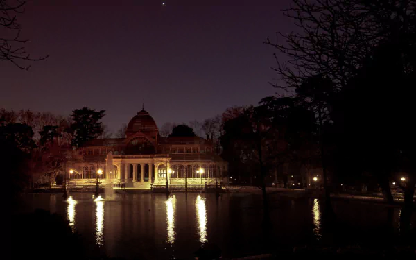 Night view of the man-made Palacio de Cristal illuminated by warm lights, reflected in the pond — HD PC desktop wallpaper and background.
