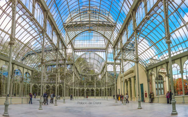 HD PC desktop wallpaper of Palacio de Cristal's ornate glass-and-iron interior, wide panoramic view of the man-made conservatory with visitors beneath a bright blue sky.