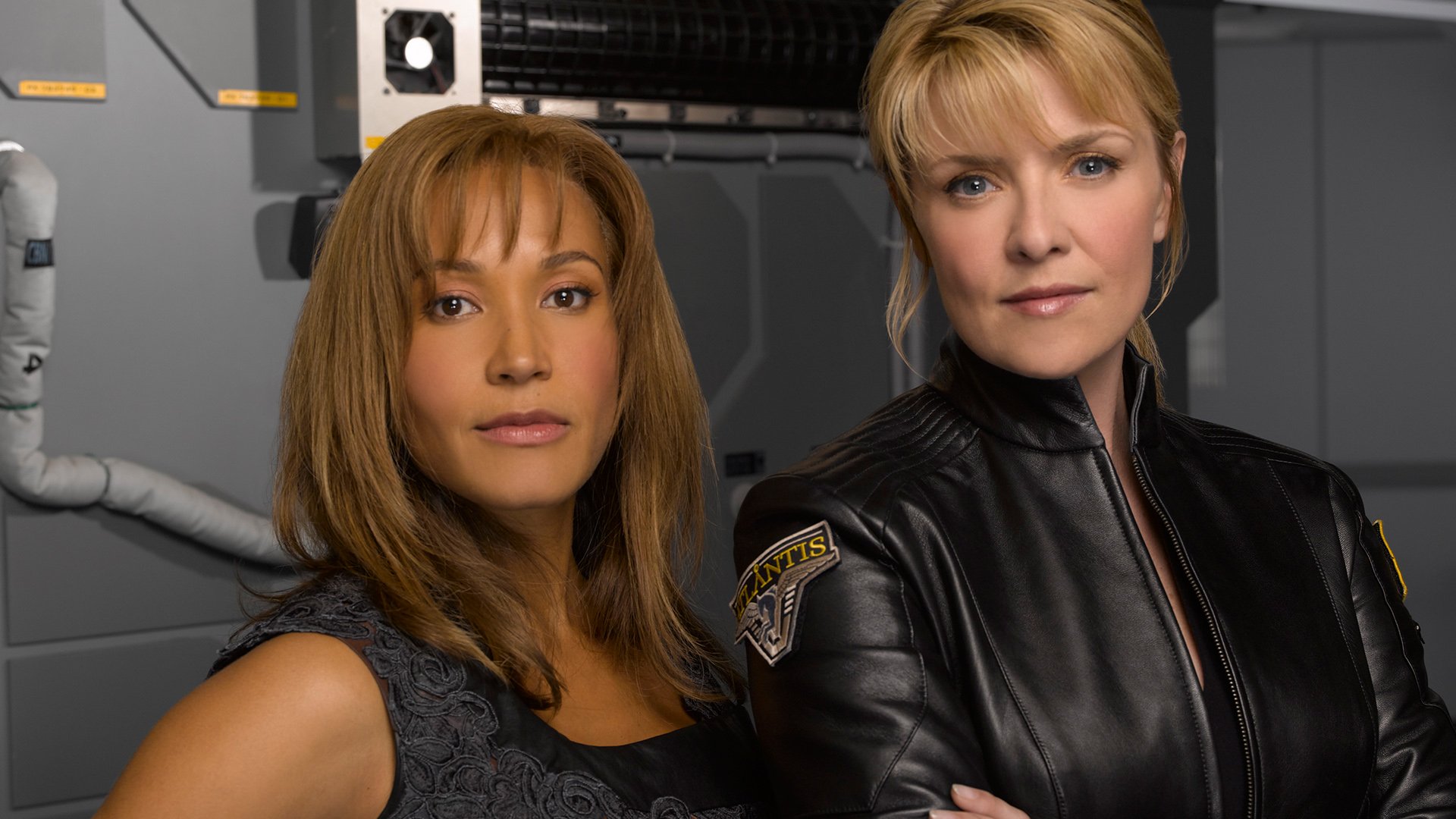 HD desktop wallpaper of two female characters from the TV show Stargate Atlantis posed against a ship-like control room background