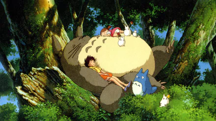 A vibrant HD wallpaper featuring Satsuki and Mei Kusakabe relaxing on Totoro's belly, surrounded by Mini Totoros in a lush green forest from *My Neighbor Totoro*.