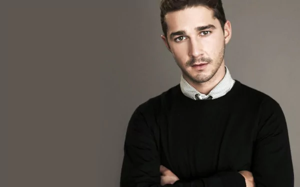 HD desktop wallpaper featuring a portrait of a man in a black sweater and white-collared shirt with a serious expression, set against a gray background.