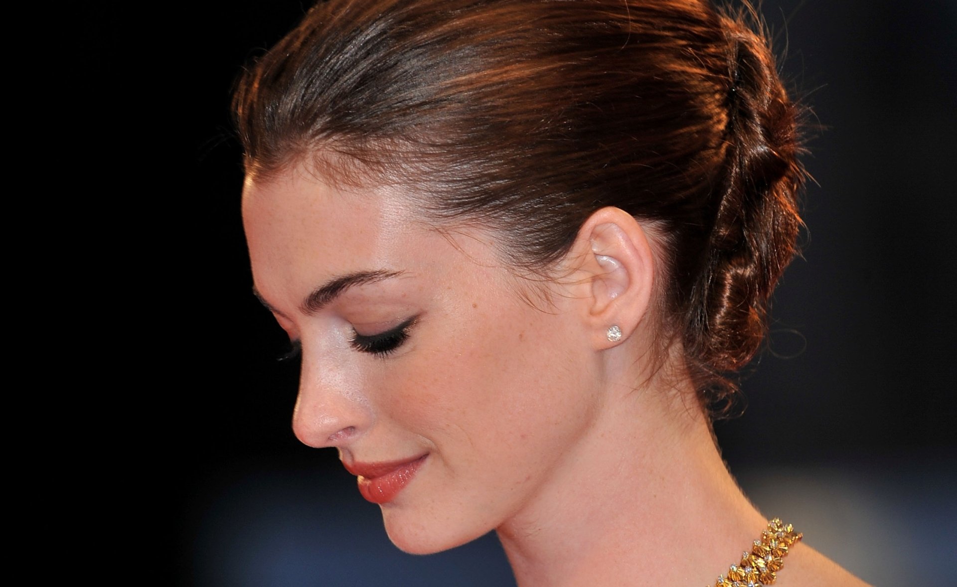 HD PC desktop wallpaper featuring a close-up profile of celebrity Anne Hathaway with elegant makeup and a braided updo against a dark background.