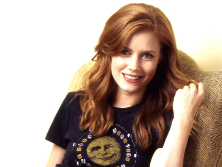 HD desktop wallpaper featuring a smiling woman with red hair, seated in a beige chair, wearing a black t-shirt.