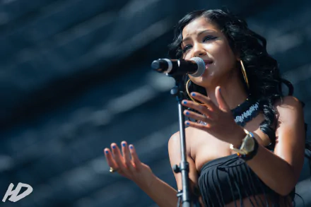 HD desktop wallpaper featuring Jhené Aiko singing into a microphone with an expressive gesture, set against a blurred background.