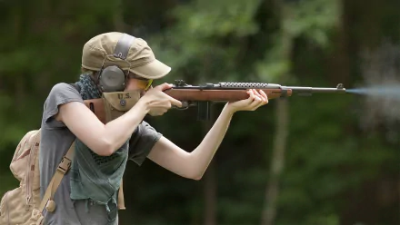 HD PC desktop wallpaper: person in cap and ear protection aiming a man-made rifle against a blurred forest background.