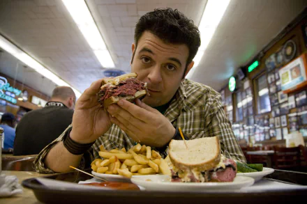 HD wallpaper featuring a scene from Man v. Food with a man ready to eat a large sandwich at a diner, with fries on the side.