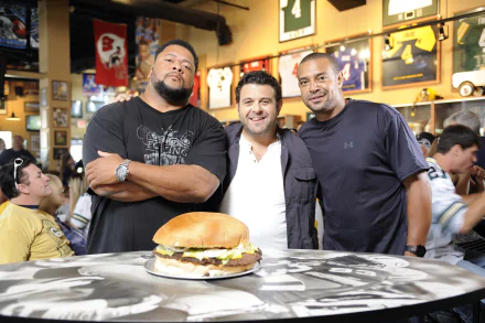 HD desktop wallpaper of Man v. Food featuring Adam Richman with two companions, in front of a giant burger at a restaurant.