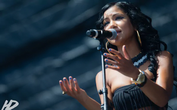 HD desktop wallpaper featuring Jhené Aiko singing into a microphone with an expressive gesture, set against a blurred background.