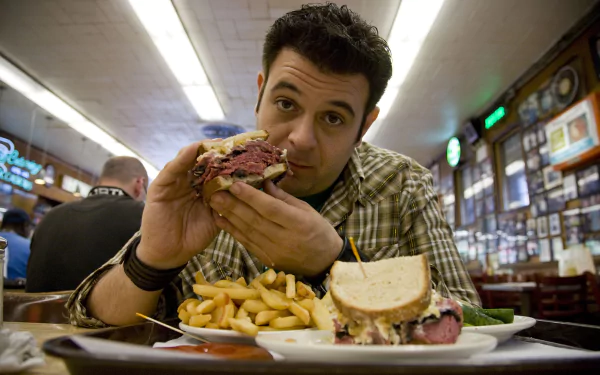 HD wallpaper featuring a scene from Man v. Food with a man ready to eat a large sandwich at a diner, with fries on the side.