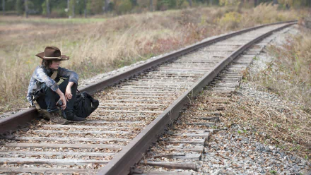 HD PC desktop wallpaper featuring a scene from The Walking Dead TV show with a character sitting alone on railroad tracks in a rural setting.