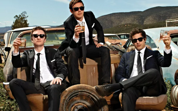 HD desktop wallpaper featuring The Lonely Island group in suits, lounging on an old car with drinks in hand.