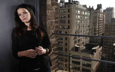 HD desktop wallpaper featuring American actress and celebrity Jaimie Alexander standing against a brick wall with a cityscape background.