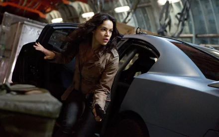 Michelle Rodriguez as Letty Ortiz in a dynamic scene from Fast & Furious 6, emerging from a sleek car in a high-octane setting. HD wallpaper captures the action-packed essence of the film.