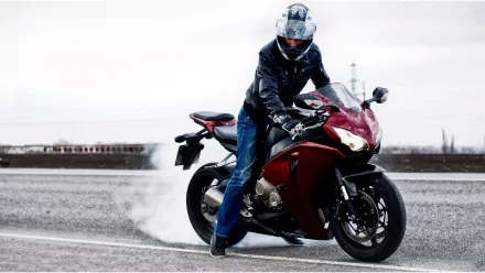 A motorcyclist performs a burnout on a sleek red bike, showcasing dynamic movement against an open road backdrop. This HD image captures the thrill of motorcycle culture.
