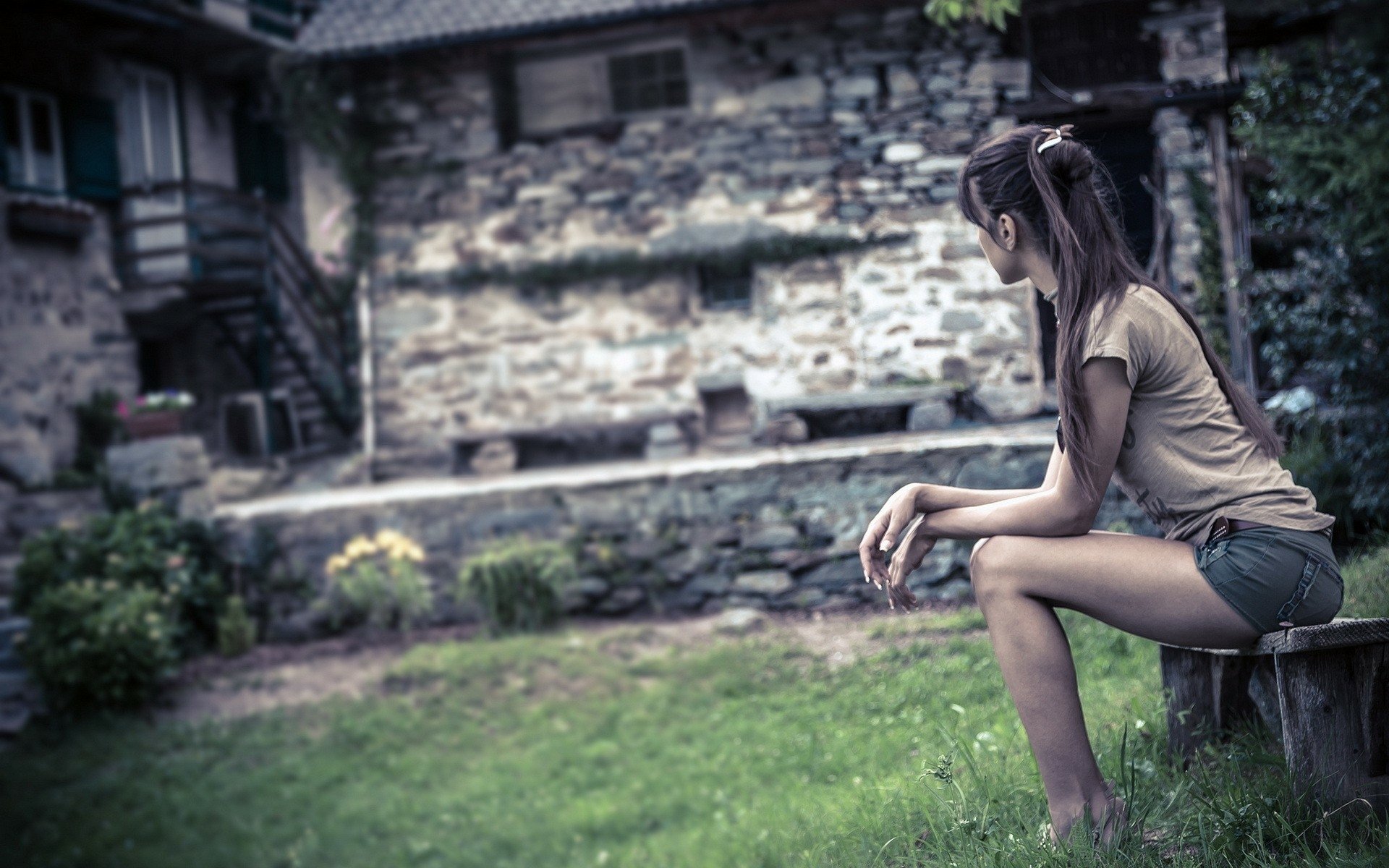 A woman sits thoughtfully on a bench in a rustic, stone-walled garden. This HD desktop wallpaper captures an artistic and serene outdoor scene.