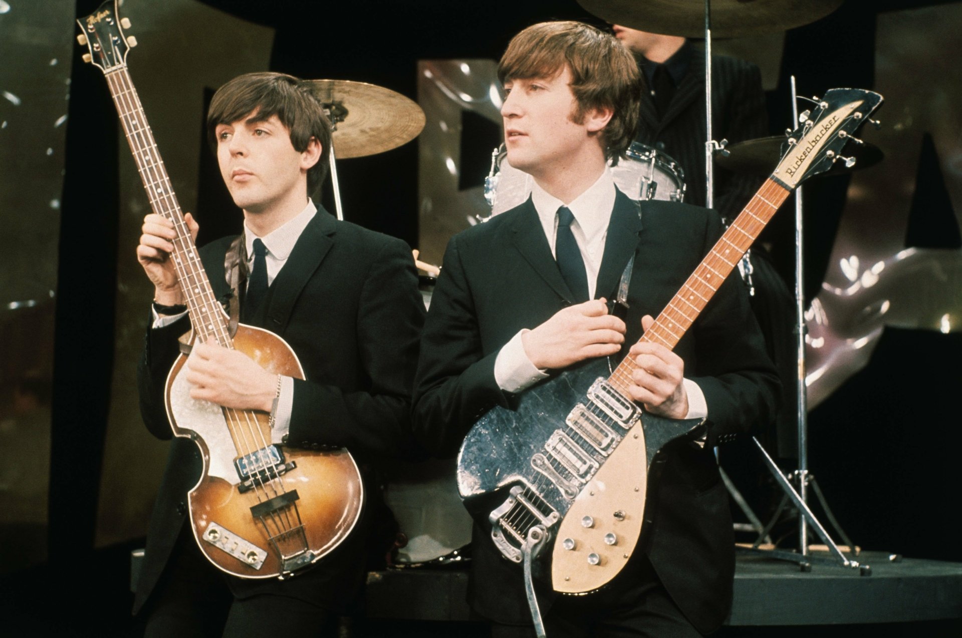 An ultra HD wallpaper featuring members of The Beatles performing, with Paul McCartney on bass and John Lennon holding an electric guitar, capturing the essence of iconic music history.