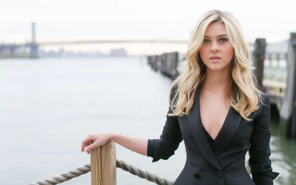 HD desktop wallpaper featuring American actress and celebrity Nicola Peltz standing by a waterfront with a city skyline in the background.