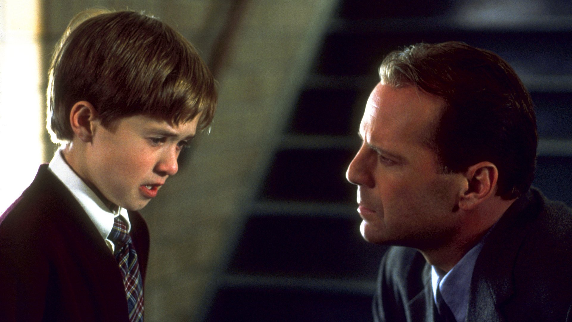 Close-up of a tense film scene: a young boy in a school uniform confronts a serious adult man on a dim staircase, cinematic HD wallpaper.
