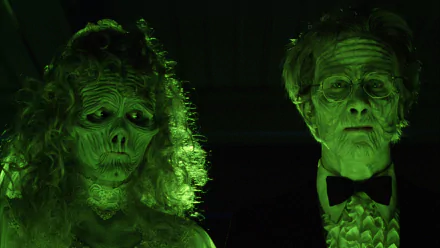 HD PC desktop wallpaper of a Beetlejuice movie scene: eerie green-lit ghosts — a skeletal, robed woman and a pale tuxedoed man — standing side by side, staring forward.