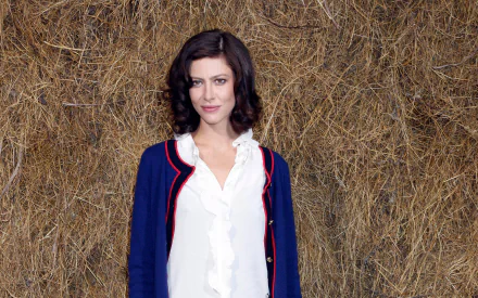 HD PC desktop wallpaper featuring actress Anna Mouglalis, standing against a textured straw background, wearing a white blouse and a navy blue jacket with red trim.