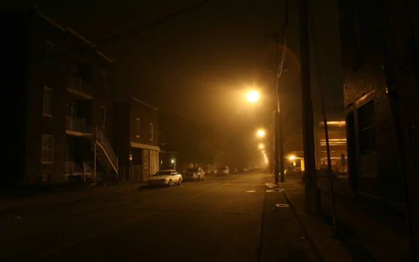 HD desktop wallpaper of a dimly lit town street at night with glowing streetlights and parked cars, showcasing a quiet, man-made urban scene.