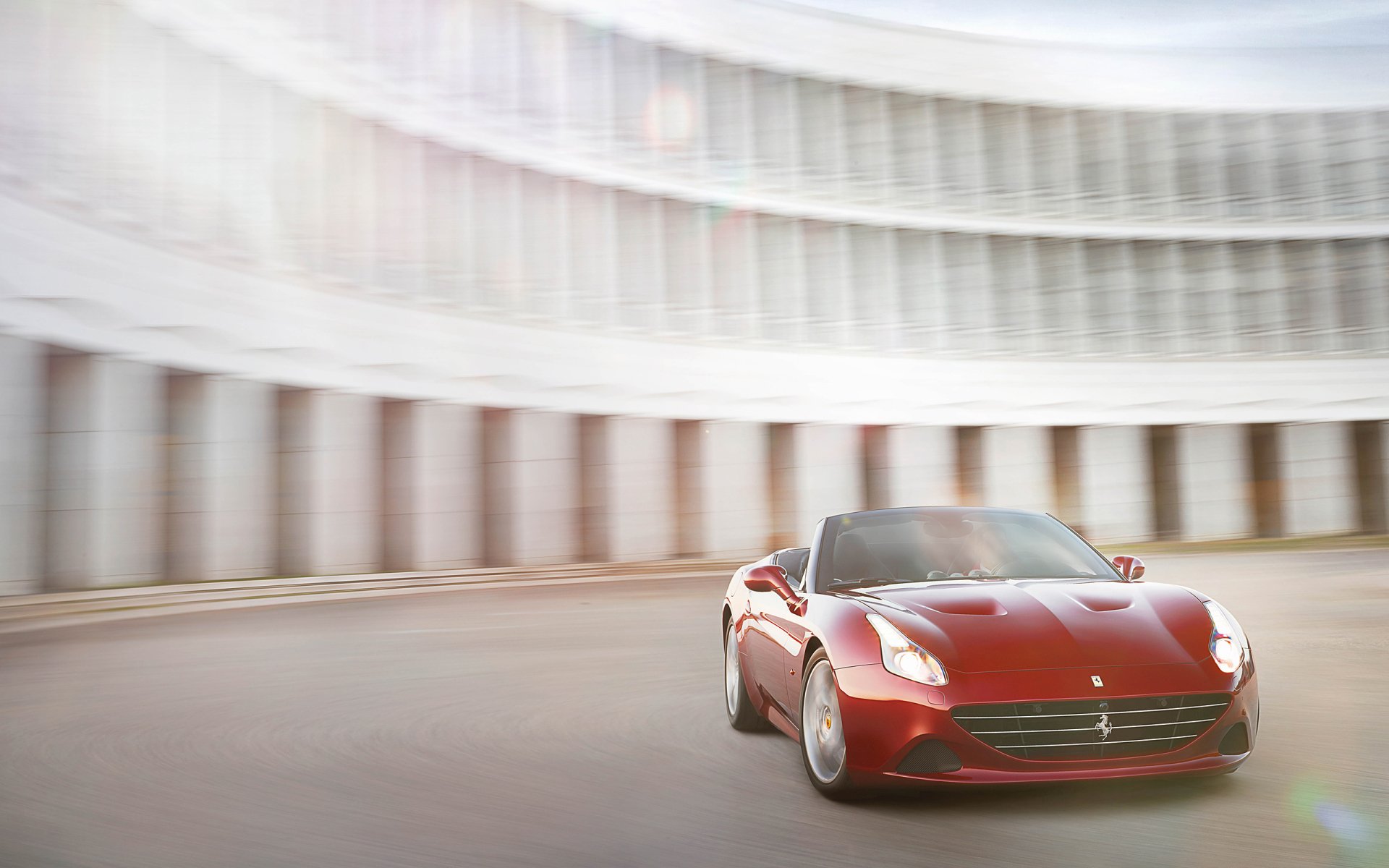 Red Ferrari California T racing past a curved colonnade with motion blur — 2K Quad HD PC desktop wallpaper of the vehicle.