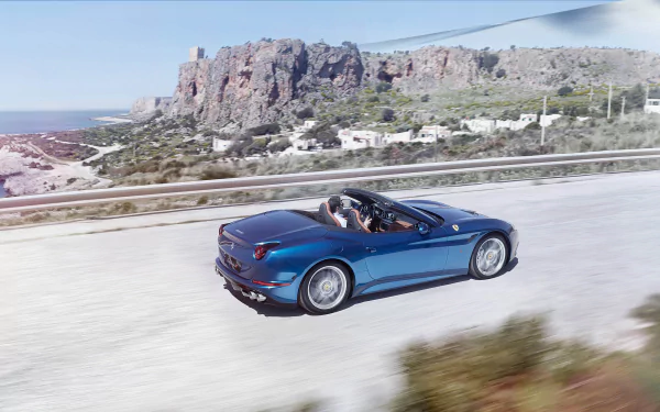 Blue Ferrari California T convertible driving past coastal cliffs; 2K Quad HD PC desktop wallpaper background showing the vehicle.