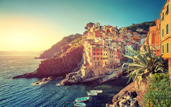 Sunset view of colorful man-made buildings in Riomaggiore, Cinque Terre, Liguria, Italy, perched on rugged coastline overlooking the sea.