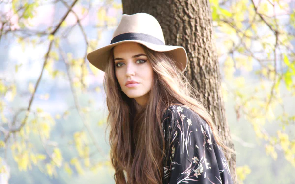 HD PC desktop wallpaper of Spanish woman Clara Alonso wearing a hat, posed outdoors by a tree with soft natural light and a blurred background.
