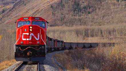 A vibrant red CN train travels along a scenic railway, surrounded by autumn foliage, making for an engaging HD PC desktop wallpaper and background.