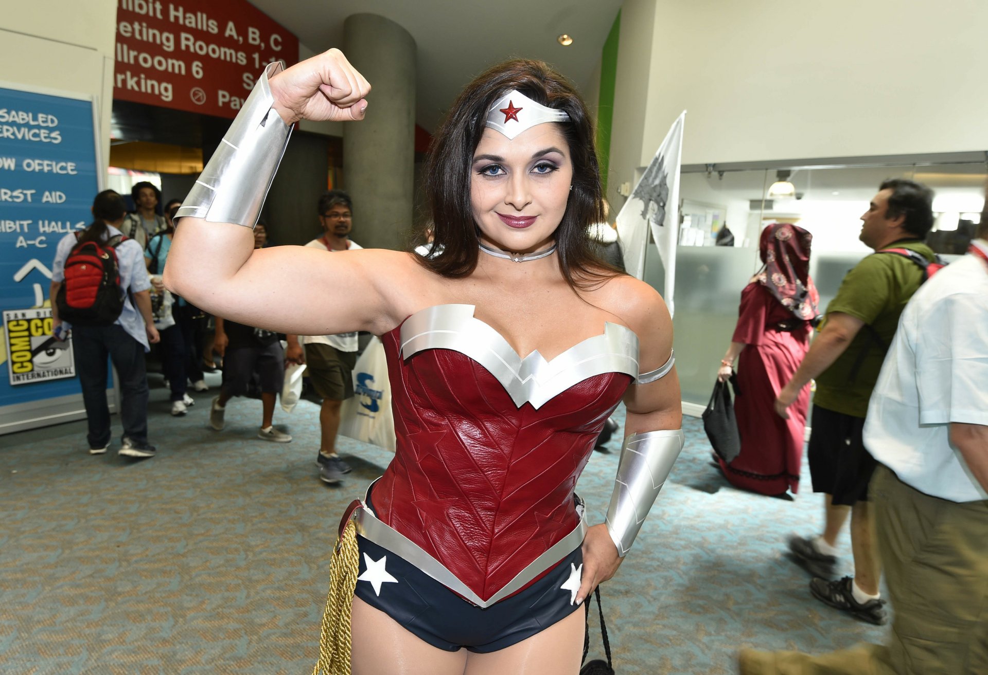 HD PC desktop wallpaper featuring a confident woman in detailed Wonder Woman cosplay at a busy convention.