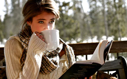 A woman, tagged as Taylor Marie Hill, enjoys a hot beverage and reads a book in a scenic outdoor setting. This HD desktop wallpaper and background highlights a cozy moment amidst nature.