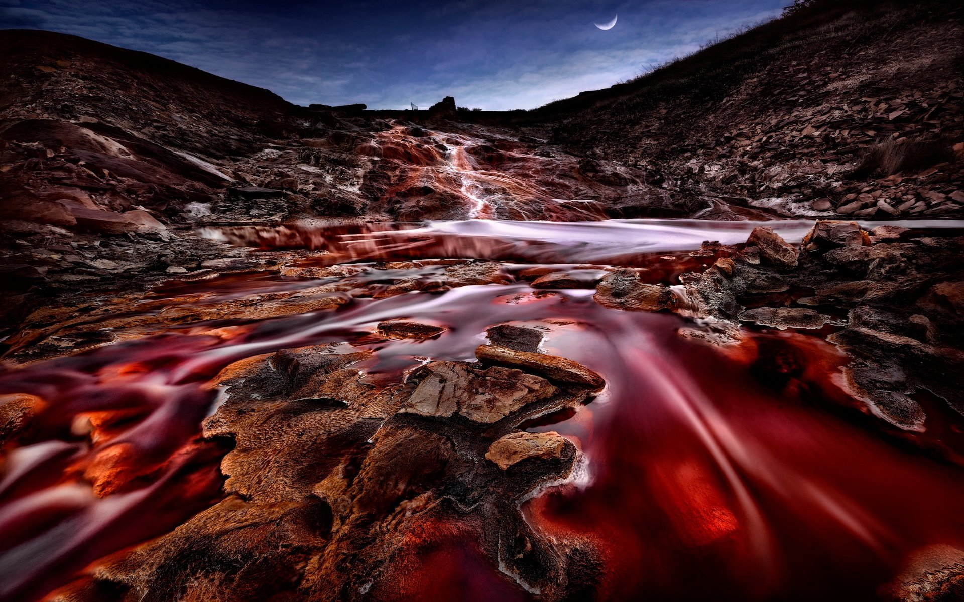HD PC desktop wallpaper background: a nature stream of deep red water flowing over jagged rocks through a twilight valley beneath a crescent moon.