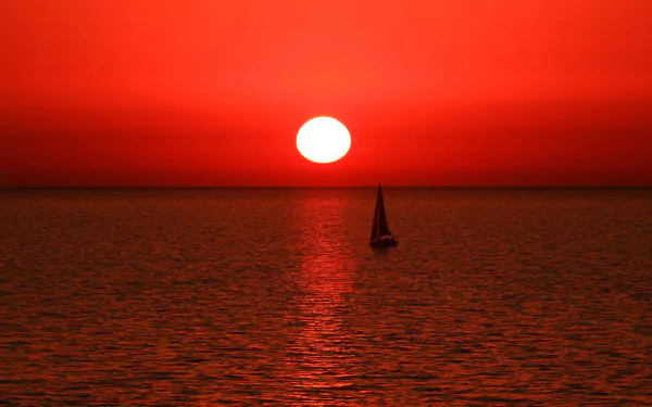 HD PC desktop wallpaper and background: lone sailboat vehicle silhouetted on a red-orange sea as the sun sets on the horizon.