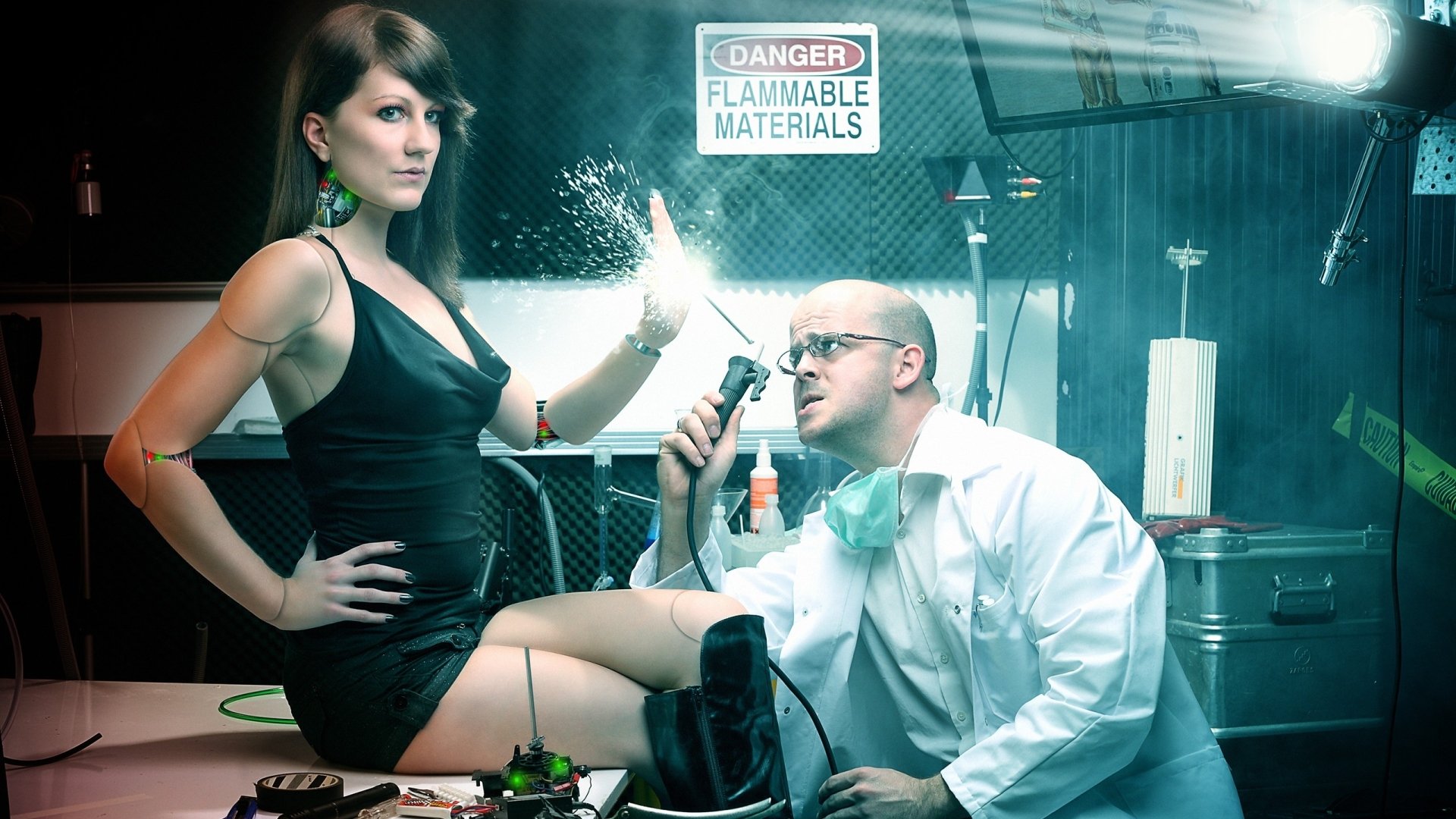 A sci-fi scene featuring a cyborg woman interacting with a scientist in a lab setting. The backdrop includes a warning sign, enhancing the futuristic atmosphere. HD desktop wallpaper.