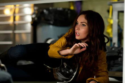 HD PC desktop wallpaper from the movie Teenage Mutant Ninja Turtles (2014): a woman in a yellow jacket crouches behind debris, tense expression in a dim, industrial garage setting.