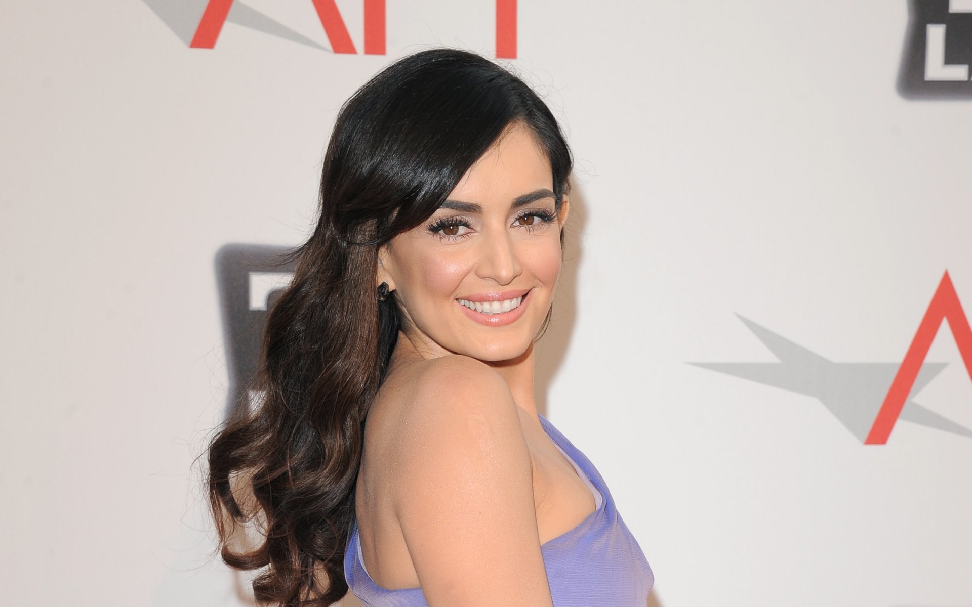 HD desktop wallpaper featuring Mexican actress and celebrity Ana de la Reguera smiling at a red carpet event with elegant wavy hair and a purple dress.