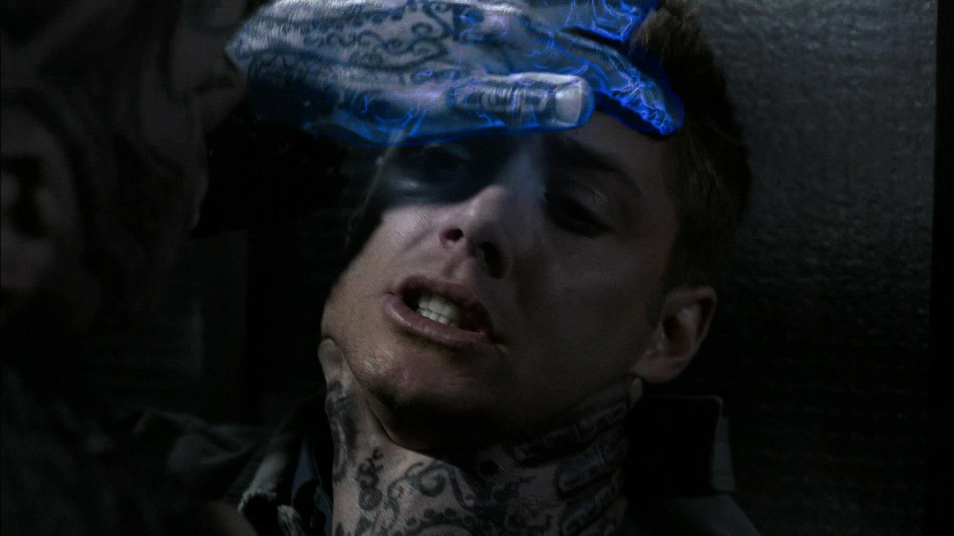 A dramatic scene from the TV show Supernatural, featuring a character with intricate tattoos, conveying an intense moment of supernatural interaction against a dark background.