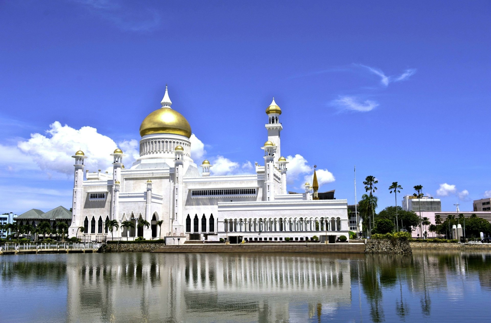 Sultan Omar Ali Saifuddin Mosque with golden domes reflects in water under a clear blue sky in Bandar Seri Begawan, Brunei.