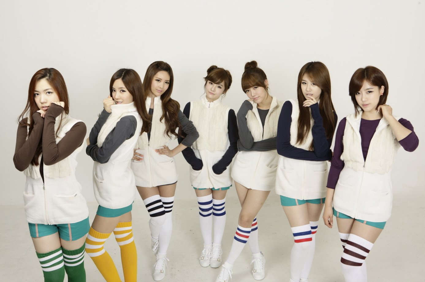 HD PC desktop wallpaper of seven women in coordinated white vests and colorful striped knee-high socks, posing together in a music-themed pop group photo.