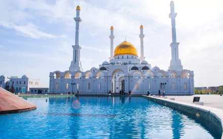 HD PC desktop wallpaper of the Nur-Astana Mosque, featuring its golden dome and tall minarets reflected in a clear blue pool under a bright sky.