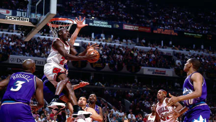 Michael Jordan soars for a slam dunk during a Chicago Bulls game, showcasing his athleticism and skill amidst a crowded arena, capturing the essence of competitive basketball.
