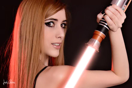 A woman poses in cosplay, confidently wielding a glowing lightsaber against a dark backdrop. This striking image is captured in 4K Ultra HD, making it a vibrant desktop wallpaper.