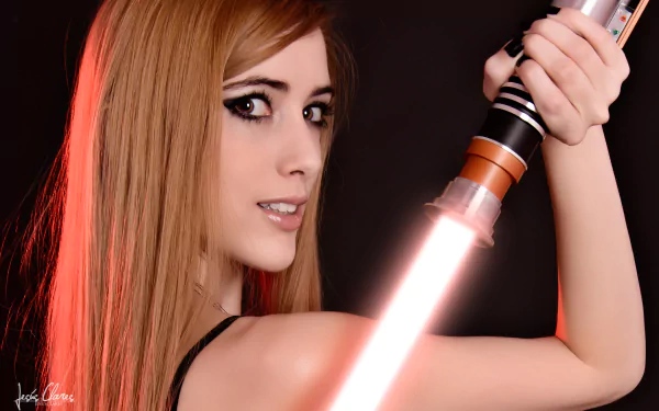 A woman poses in cosplay, confidently wielding a glowing lightsaber against a dark backdrop. This striking image is captured in 4K Ultra HD, making it a vibrant desktop wallpaper.