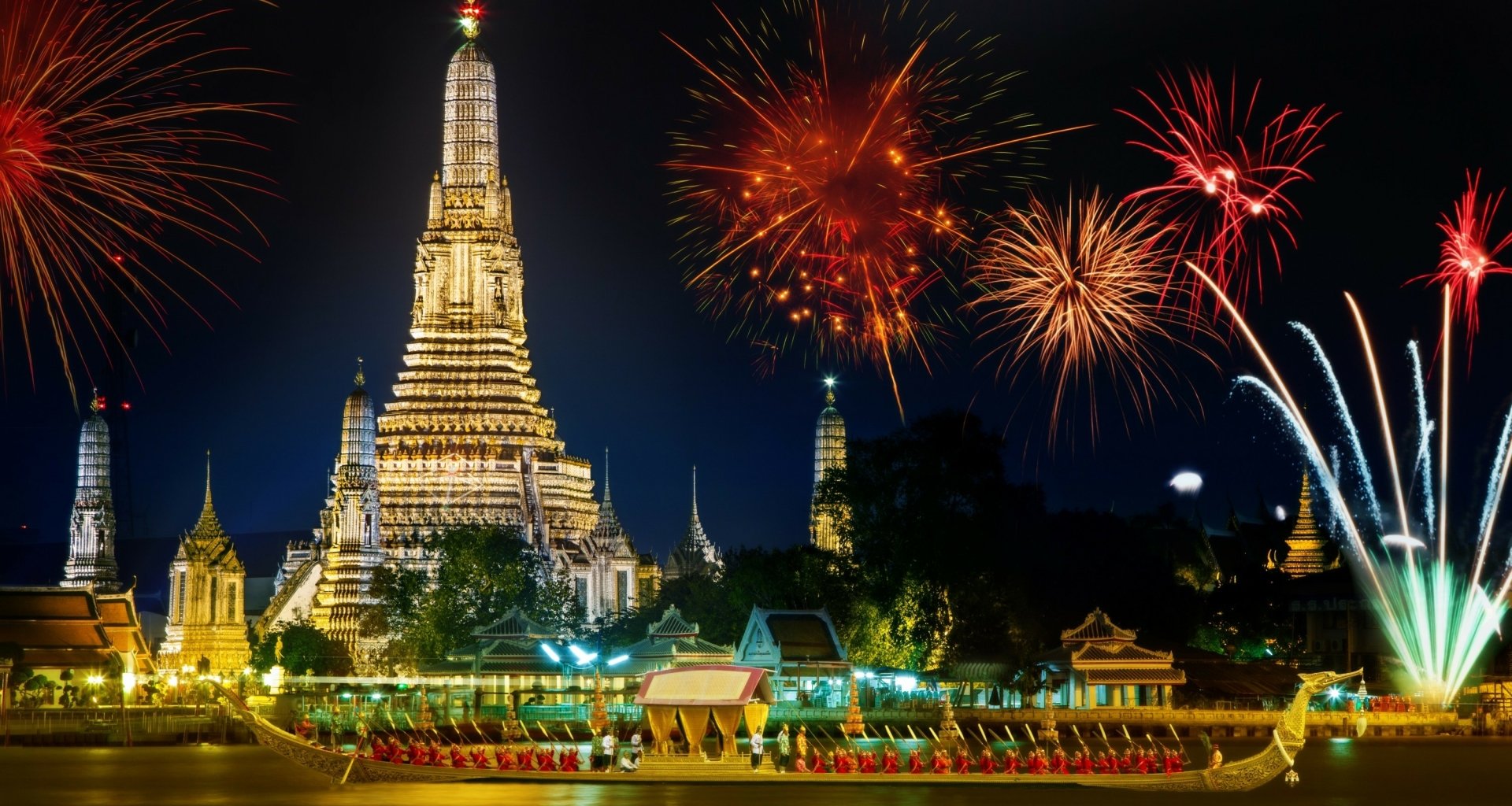 Night view of the illuminated Wat Arun Temple in Bangkok, Thailand with vibrant fireworks lighting up the sky, captured in a striking HD desktop wallpaper.